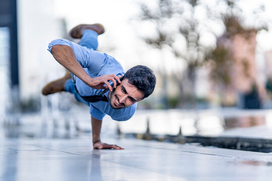 Smiling businessman talking on mobile phone while doing handstand on footpath