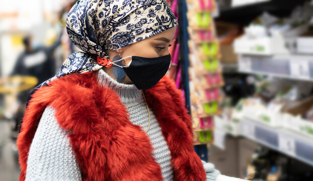 Young woman wearing headscarf and protective face mask shopping while standing at supermarket