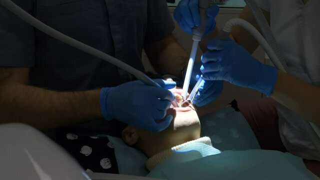 professional dentist drills tooth an assistant holds salivating pump patient lies in chair with glasses under lamp