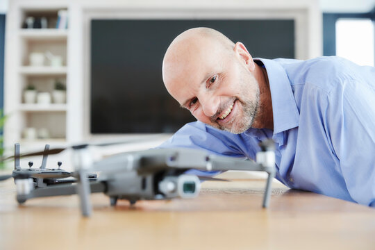 Smiling businessman examining quadcopter while standing at home