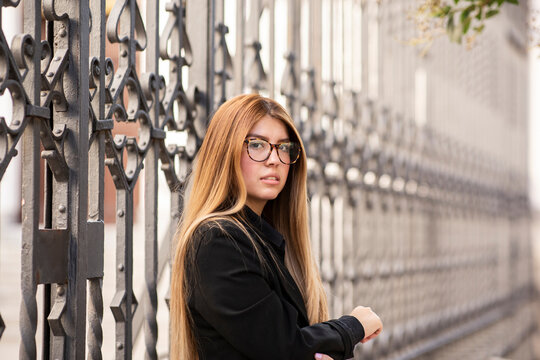Young woman wearing eyeglasses standing against gate