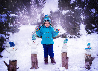 child playing in snow. Little girl in a blue coat and four little snowmen on a snowy background. Copy space. Winter fun.