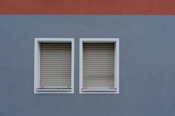 Blue wall with red stripe, two windows with  aluminum shutter, jalousie rolled up symbol for lockdown, no person