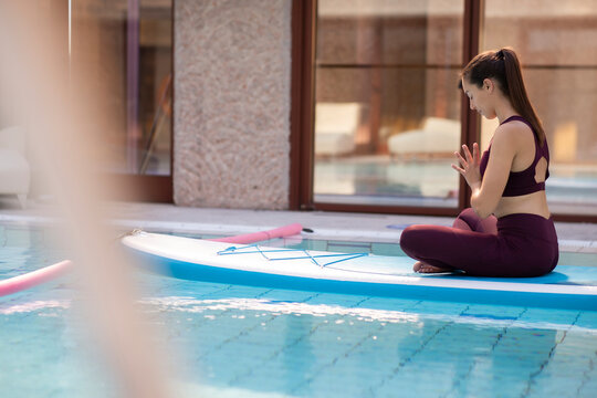 Female instructor practicing yoga on paddleboard over swimming pool