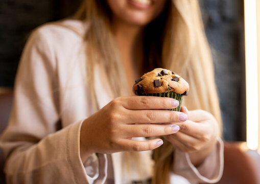 Woman holding chocolate chip muffin while sitting at cafe