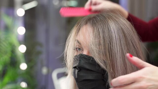 in a beauty salon the hands of a hairdresser cut the blonde hair of a girl in a black protective mask. cut hair falls down