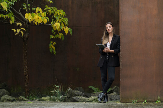 Young beautiful female entrepreneur holding digital tablet while leaning on brown wall
