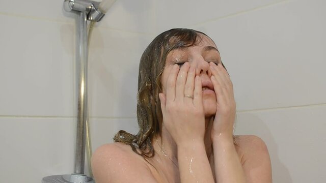 Young charming woman washes off mascara from her eyes in the shower