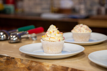 A delicious British cup cake with white icing and multi coloured sprinkles on a white plate