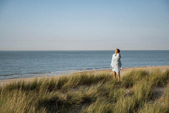 Young woman wrapped in shawl standing at beach