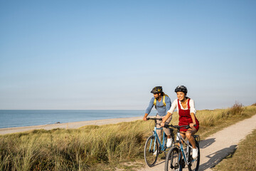 Smiling woman wearing cycling helmet riding bicycle with man against clear sky