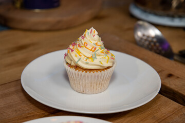 A delicious British cup cake with white icing and multi coloured sprinkles on a white plate
