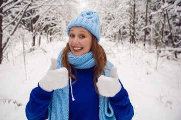 woman in a blue tracksuit white mittens and scarf stands in winter in a snow covered forest