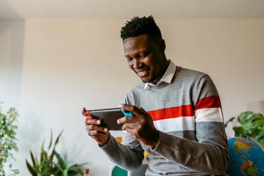 Smiling businessman playing on handheld video game at home during break from work