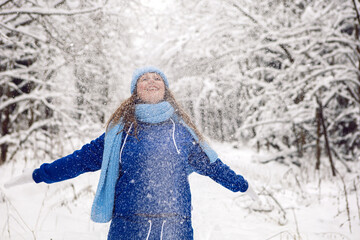 woman in a blue tracksuit white mittens and scarf stands in winter in a snow covered forest