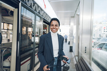 Happy businesswoman with mobile phone at bus stop during COVID-19 outbreak