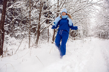 Fototapeta na wymiar woman in a blue tracksuit white mittens and scarf stands in winter in a snow covered forest