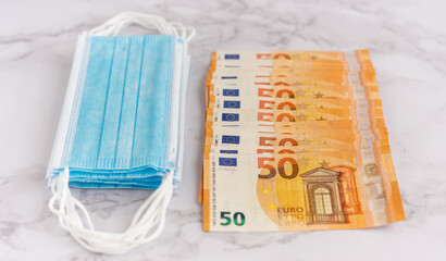Medical masks and euro bills on a marble background, the concept of expenditure on masks that have been made in the context of the global COVID-19 pandemic. Selective Focus