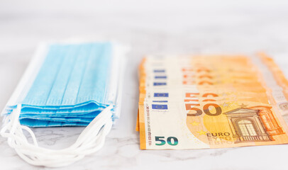 Medical masks and euro bills on a marble background, the concept of expenditure on masks that have been made in the context of the global COVID-19 pandemic and the fight against the coronavirus.