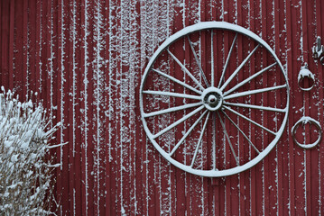 An old wheel hanging on an old buildings wooden wall in wintertime