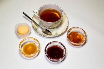 A cup of strong tea, rosettes with raspberry jam, apples and honey. White background.