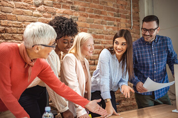 . Group of young confident business people analyzing data using computer while spending time in the office. Business people are using gadgets, talking and smiling during the conference in office