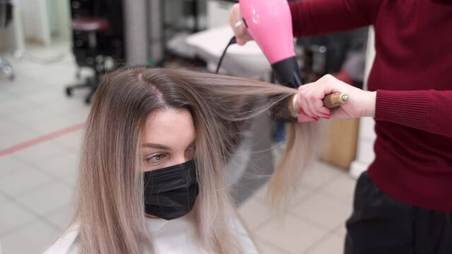 a girl in a black mask blow-dry her hair by pulling it through a round brush