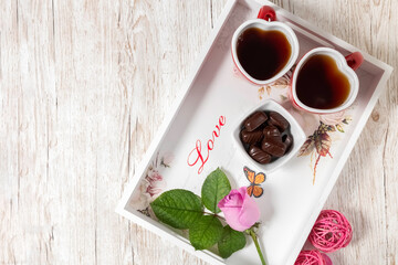 Two red cups with tea on a white tray. Breakfast for lovers. Heart shaped cup. Valentine's Day. Chocolates in a vase. Postcard. View from above.