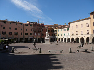 Fototapeta na wymiar Piazza Dante is the main square of Grosseto with porticos of historic palaces in the background and in the center the statue to Canapone.