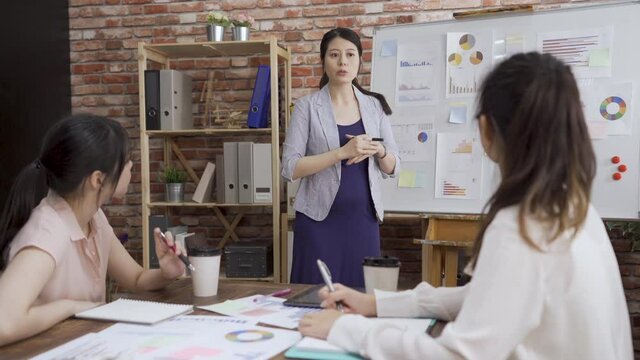 creative female people doing brainstorming meeting in modern studio. three young business women in boardroom discussing new plan. pregnant lady manager giving report to girl employee in office.