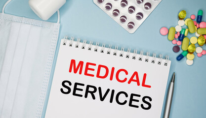 MEDICAL SERVICES is written in a notebook on a blue background next to pills, mask and pen.