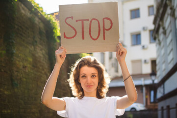 Young protesting woman in white shirt and jeans holds protest sign broadsheet placard with slogan...