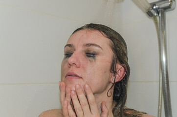 Young charming woman washes off mascara from her eyes in the shower