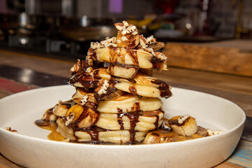 A delicious plate of Banoffee Pecan and Chocolate Pancakes draped in Chocolate and toffee source, on a wooden kitchen table