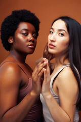 young pretty asian and afro woman posing cheerful together on brown background, lifestyle diverse nationality people concept