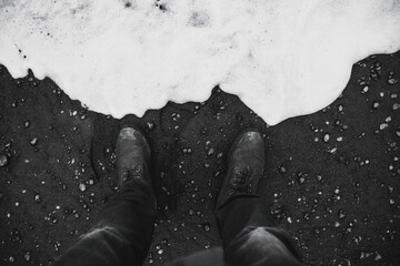 Grayscale shot of dirty shoes standing on the sandy beach with waves