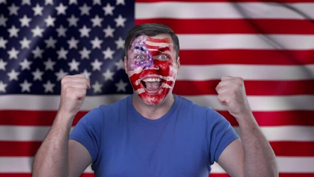 A screaming Caucasian cheerleader against the background of the US flag with a painted face in national colors.