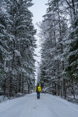 A lonely girl in a yellow jacket on a snowy road going into the distance.