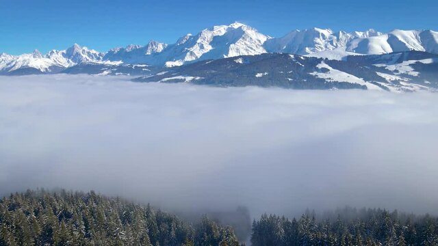 Mont Blanc summit with scenic white winter alpine landscape viewed from Meg&egrave;ve, snow covered Alps mountains with coniferous forest and sea of clouds, 4k aerial video from drone near Chamonix, France