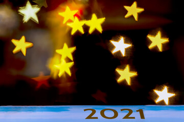 The golden inscription 2021 on a celestial background against a dark background with bokeh of star-shaped lights