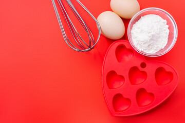 Whisk, red silicone mold and ingredients for a dessert on a festive table on Valentine's Day.