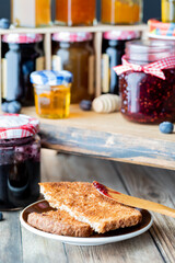 Toast with raspberry jam on a spreader and jars of jam in soft focus in behind.