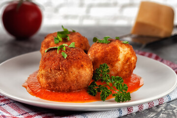 Delicious hot italian arancini - rice balls stuffed with cheese in tomato sauce, in a plate on an old wooden table