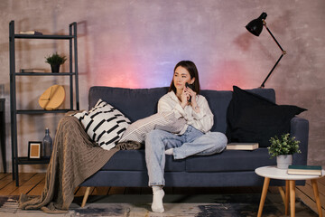 Young asian woman sitting on a sofa in a cozy room looks at the phone