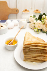 A stack of thin pancakes, folded in corners, drizzled with honey on a white plate.
