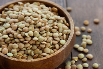 Uncooked raw green lentil in bowl on wooden background, (Lens culinaris)