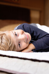 Happy little boy lying don on bed and looking at camera.