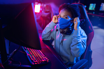 Hosting online video game tournaments computer clubs during pandemic, American African young woman wearing protective mask against Covid