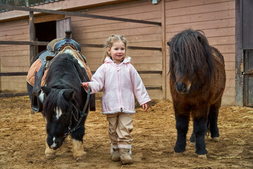 Girl and pony. Child and horses on the farm in the paddock. Equestrian school. Hippotherapy at the...