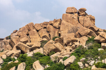 Hampi, Karnataka, India - November 5, 2013: Brown stone boulder hill with some green weeds outside...
